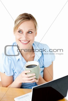 Smiling businesswoman drinking coffee using her laptop at the breakfast table