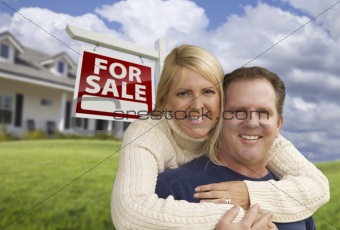 Happy Couple Hugging in Front Yard with Real Estate Sign and House.
