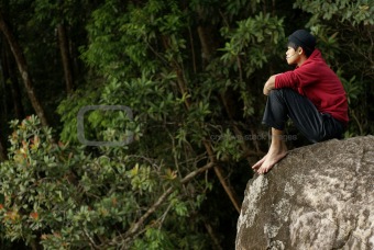 Lonely asian man sitting on rock outdoors wearing cold apparel looking far away