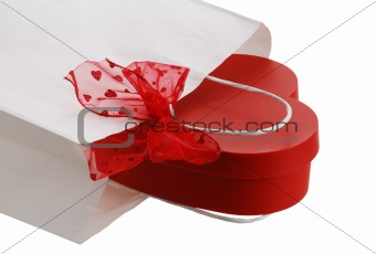 Closeup of white paper gift bag with red bow and heart shaped pr