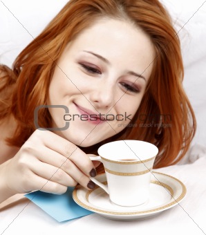 Pretty red-haired sleeping woman in white nightie lying in the bed near cup of coffee.