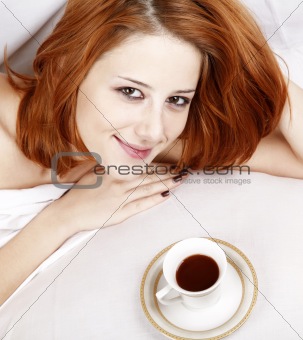 Woman in white nightie lying in the bed near cup of coffee