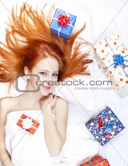 Happy red-haired girl in bed with Christmas gifts.