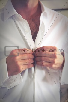 Groom buttons his shirt before the wedding