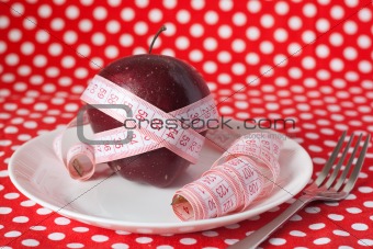 Red apple and measuring tape on a white plate