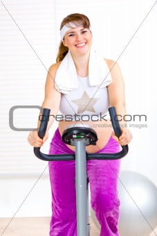Smiling beautiful pregnant woman working out on static bike
