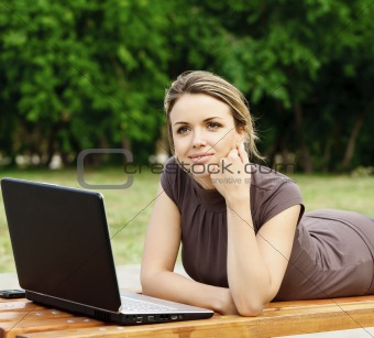 Young pretty woman with laptop lying on the bench at a park