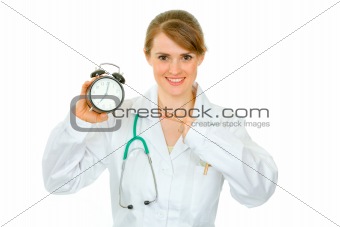 Smiling  medical female doctor pointing finger on alarm clock
