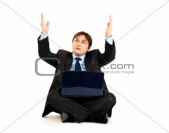 Sitting with laptop on floor businessman looking up and raising his hands
