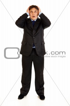 Full length portrait of shocked businessman holding hands near head and looking up
