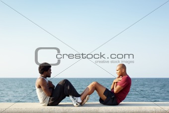 two men exercising abs near the sea