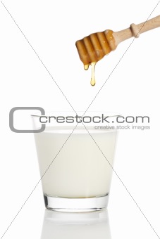 honey drops from a honey dipper in a jar with milk