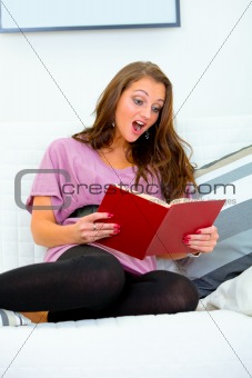 Shocked  young woman sitting on sofa and reading  book
