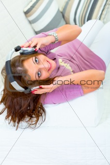 Cheerful young woman sitting on sofa and listening music in headphones
