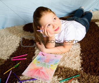 The girl lies on a carpet and thoughtfully draws 