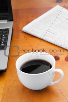 A cup of coffee with a laptop and a newspaper