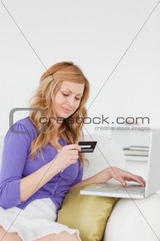 Good looking woman sitting on a sofa is going to make a payment 