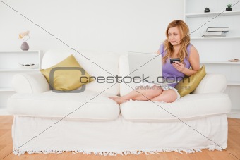 Good looking woman sitting on a sofa is going to make a payment 