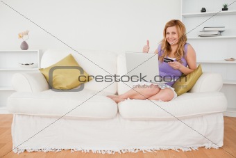 Happy woman sitting on a sofa is going to make a payment on the 