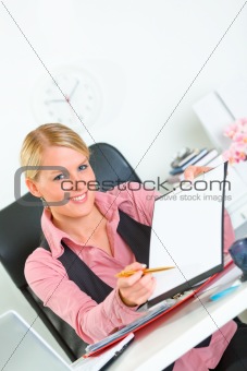 Smiling business woman sitting at office desk with document and pen for signing 

