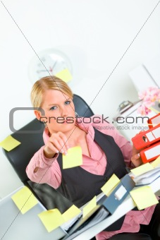 Stressful business woman sitting at workplace and stretches out hand with blank sticky notes 
