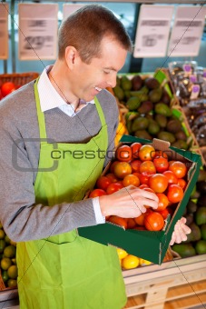 Happy market assistant holding box of tomatoes