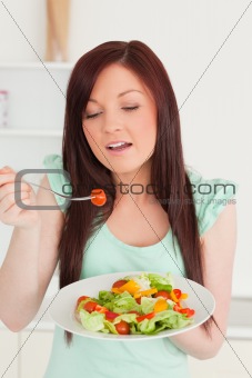 Pretty red-haired woman enjoying a mixed salad in the kitchen