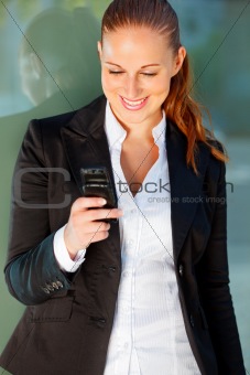Smiling business woman near office building  looking on mobile 
