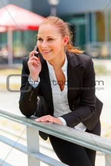 Smiling business woman leaning on railing and talking on mobile
