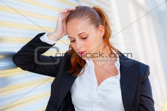 Tired business woman standing at office building and looking down
