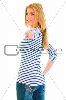 Smiling beautiful teen girl looking back and pointing finger at you
