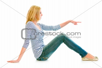 Beautiful teen girl sitting on floor and pointing finger at copy-space
