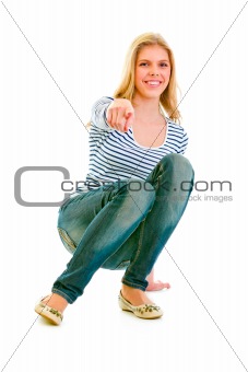Smiling beautiful teen girl squatting and pointing finger at you
