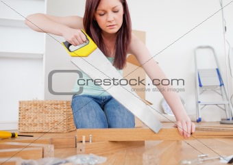 Beautiful red-haired female using a saw for diy at home