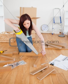 Attractive red-haired female using a saw for diy at home