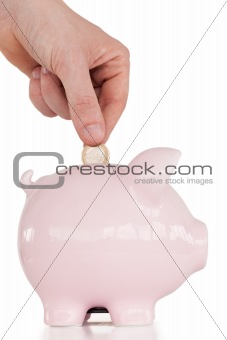 Hand inserting a coin in a pink piggy bank