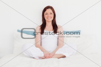 Good looking red-haired female relaxing while sitting on her bed