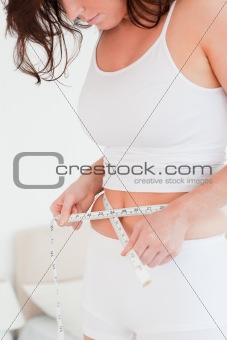 Charming brunette woman measuring her belly with a tape measure 