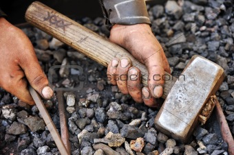 Detail of dirty hands holding hammer and rod - blacksmith