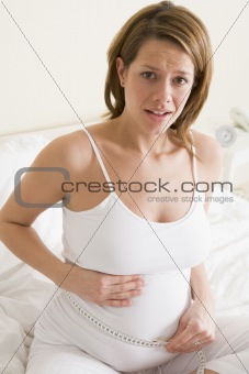 Pregnant woman in bedroom measuring belly looking worried