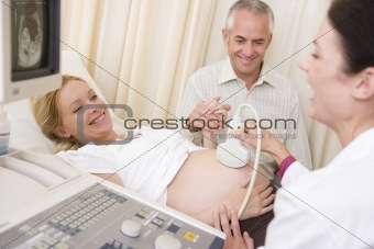 Pregnant woman getting ultrasound from doctor with husband watch