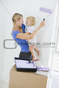 Mother holding son while painting room in new home smiling