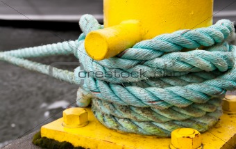 Twisted green rope around a yellow pier