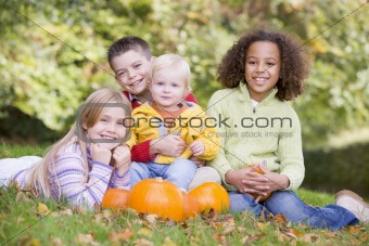 Three young friends with baby sitting on grass with pumpkins smi