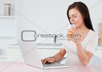 Brunette using her laptop and drinking orange juice