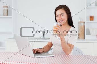 Young woman using her laptop and drinking orange juice