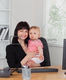 Attractive brunette woman posing while holding her baby on her k
