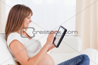 Beautiful pregnant woman relaxing with a computer tablet while s