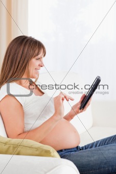 Attractive pregnant woman relaxing with a computer tablet while 