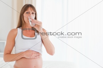 Cute pregnant female taking a pill while sitting on a bed
